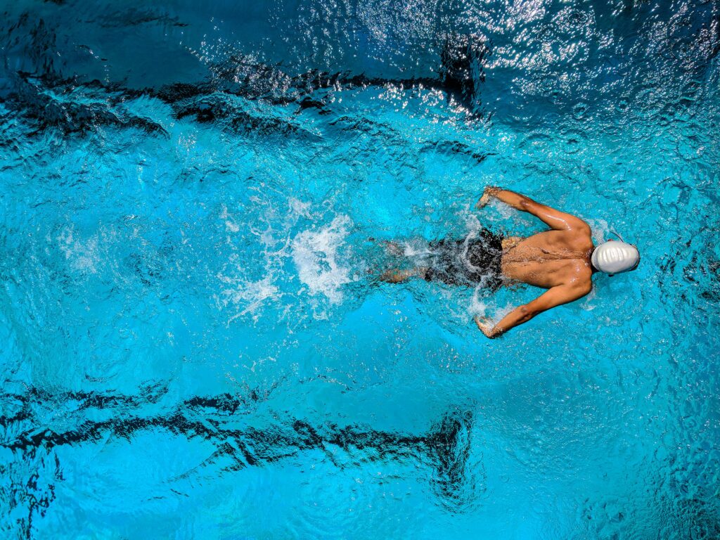pexels-photo-863988-863988 Top view of a swimmer wearing a cap, performing a front crawl stroke in a clear blue swimming pool.